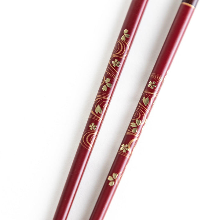 Two pairs of chopsticks, one black and one red, each adorned with intricate floral patterns on a dark background.