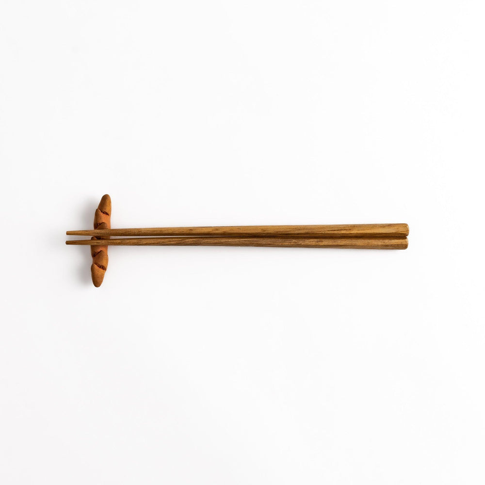 Epi Bread Chopstick Rest holding wooden chopsticks, showcasing its unique baguette design and practical functionality.