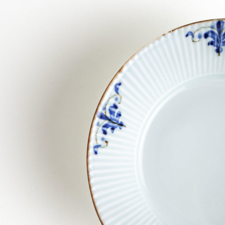 A round, shallow white bowl with blue floral patterns and a ribbed design along the edges and brown accent trim.