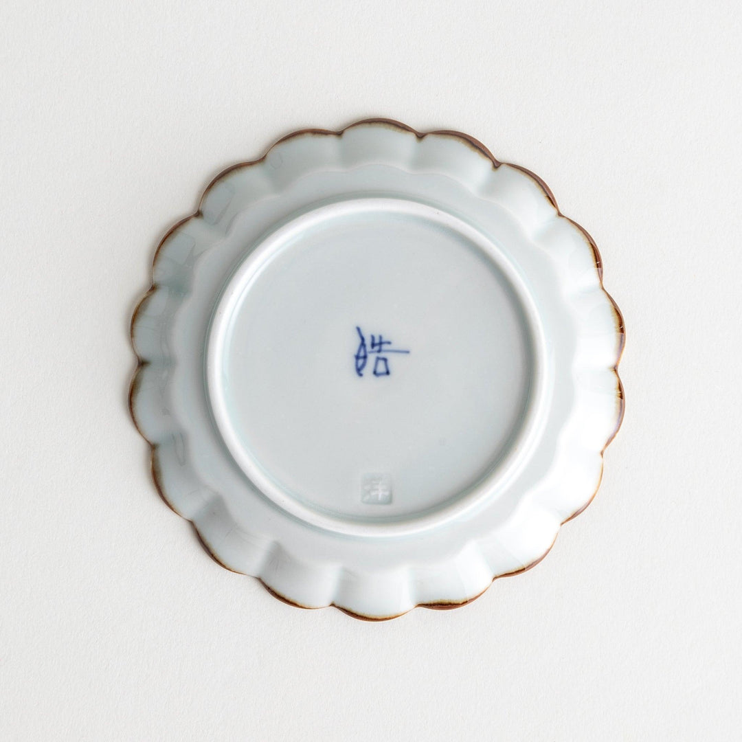 Round white porcelain sauce dish with scalloped edges, adorned with a simple blue floral pattern and brown accent trim.