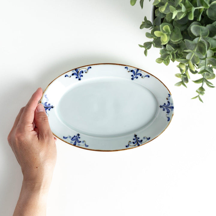 A porcelain oval salad plate, decorated with blue and white floral motifs and brown accent trim.