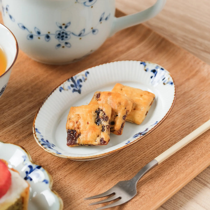 Floral Leaves Ridged Oval Sauce Dish with raisin cookies, placed on a wooden tray next to a dessert fork.