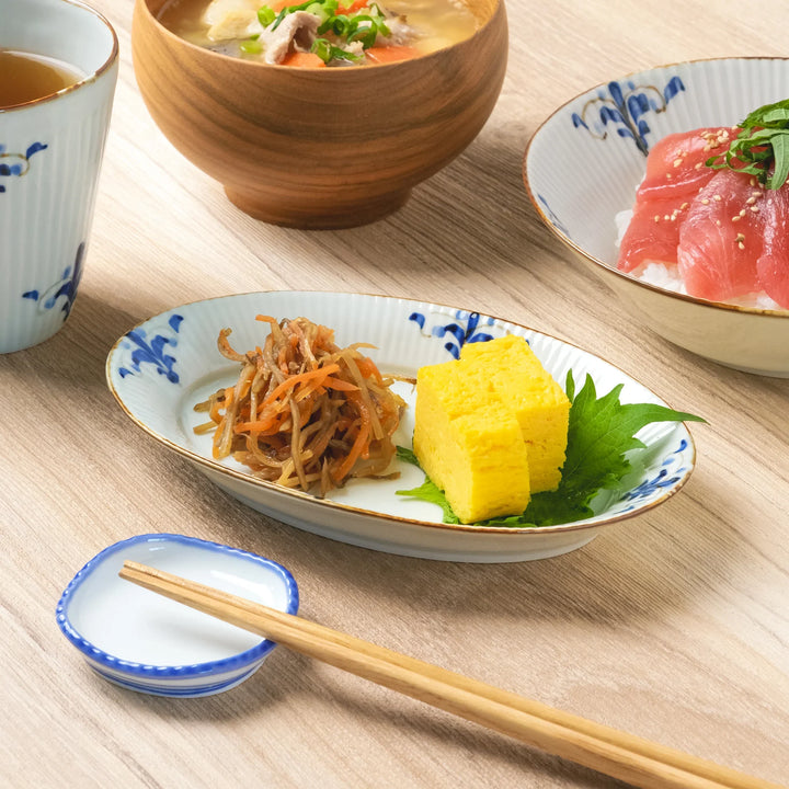 A ridged oval Japanese oval plate with blue floral leaf design, serving tamagoyaki and kinpira as part of a Japanese meal.