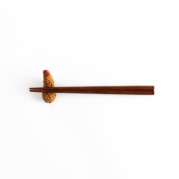 Distant view of chopsticks resting on the fried shrimp chopsticks rest, highlighting its realistic golden texture and red accent.