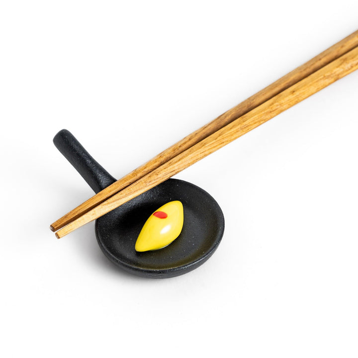 Cute frying pan-shaped chopstick rest with a yellow omelette accent, adding a fun touch to your dining experience.