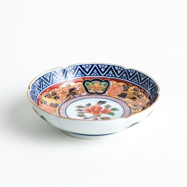 A round sauce dish with a central red floral motif, surrounded by a detailed border of gold, blue, and green floral patterns.