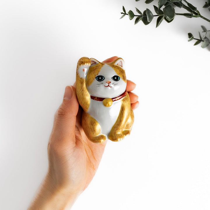Maneki Neko figurine with a golden brush design, featuring a waving cat with a collar and bell for good luck.