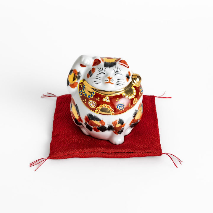 Maneki Neko figurine featuring a golden calico design, a raised paw, and a red patterned collar for good fortune.