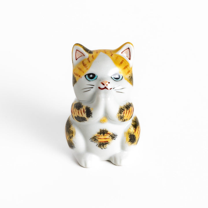 Maneki Neko figurine in a golden calico design, with a praying posture and blue eyes for good fortune.