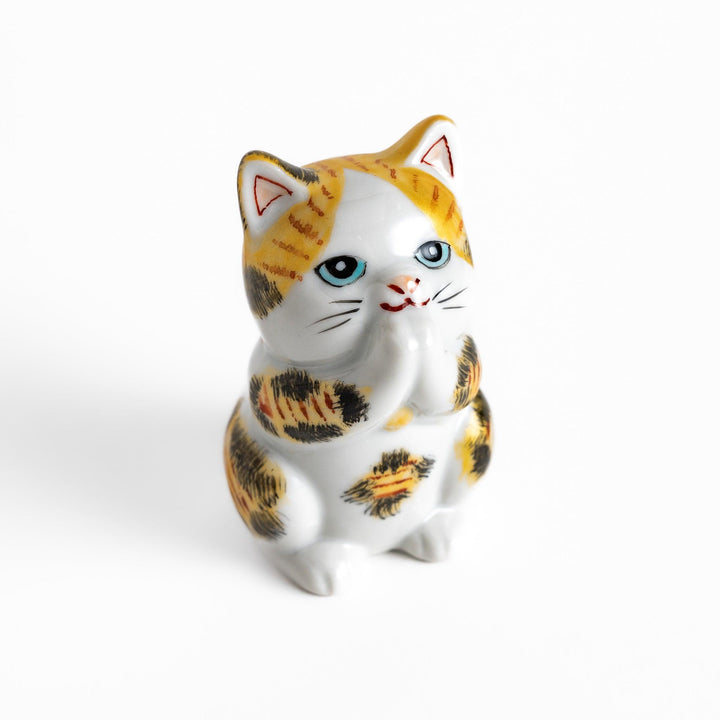 Maneki Neko figurine in a golden calico design, with a praying posture and blue eyes for good fortune.