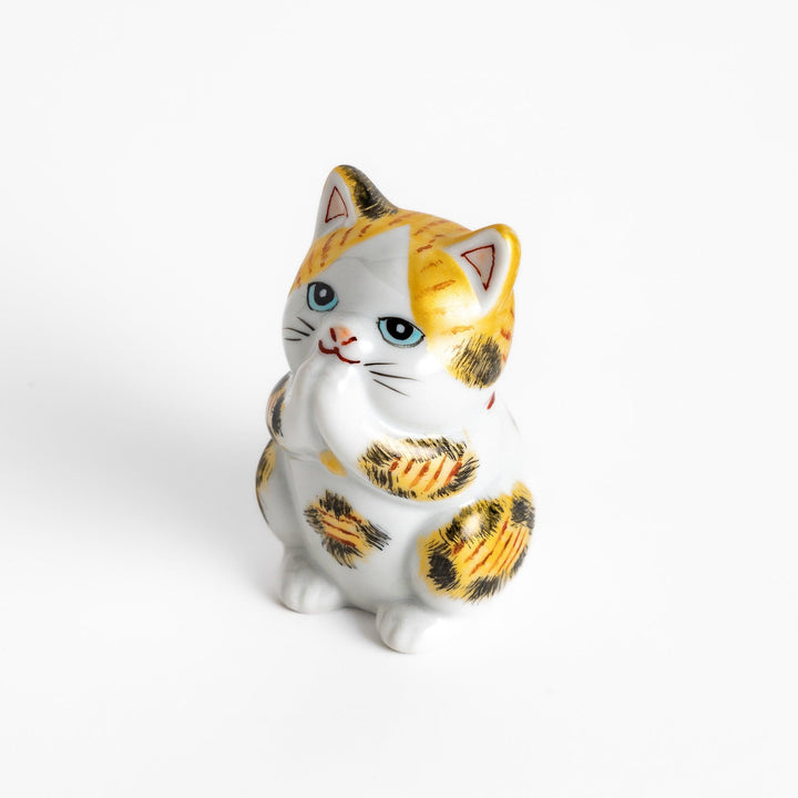 Maneki Neko figurine in a golden calico design, with a praying posture and blue eyes for good fortune.