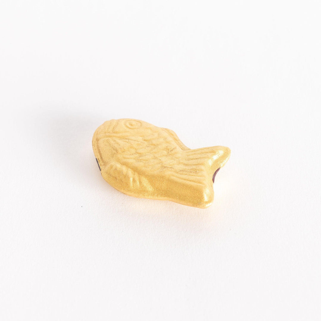 Slightly angled view of a golden taiyaki-shaped chopstick rest on a white background.