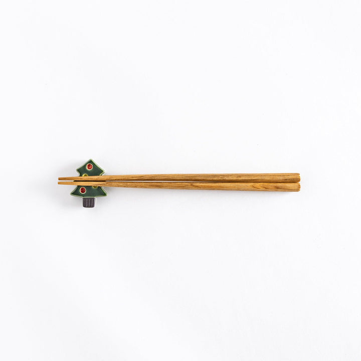 The green Christmas tree chopsticks rest with chopsticks resting on it, photographed from a distance.