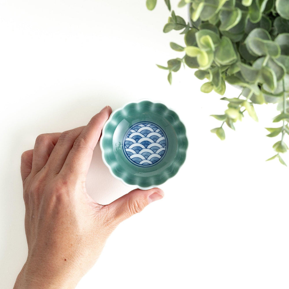 A small green cereal bowl with a scalloped edge and a blue and white wave pattern in the center.
