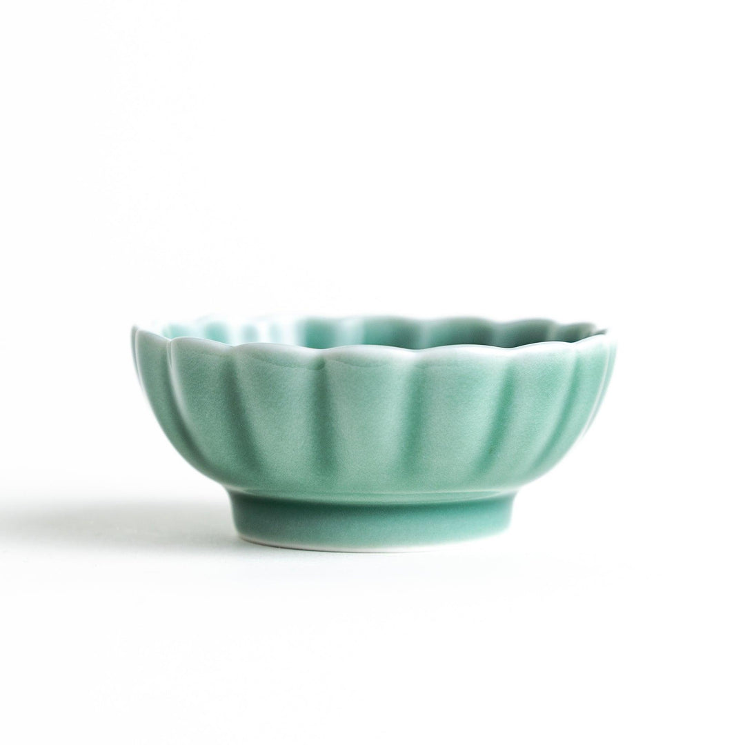 A small green cereal bowl with a scalloped edge and a blue and white wave pattern in the center.