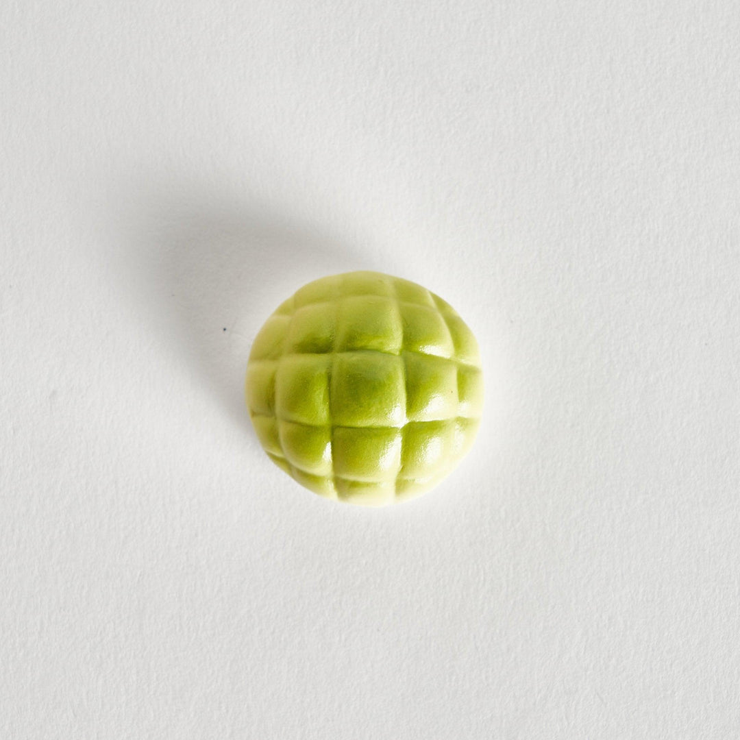 Top view of the green melon-shaped chopstick rest, showing its smooth, rounded base and a textured top resembling a melon rind.