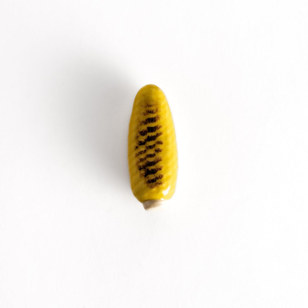 Realistic grilled corn-shaped chopsticks rest with charred detailing on its bright yellow surface, showcasing playful and lifelike design.