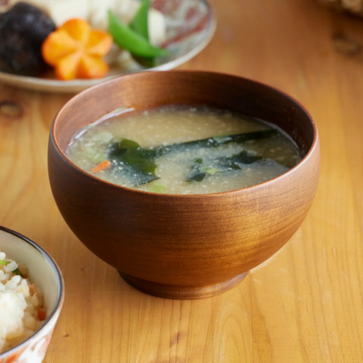 Medium handcrafted cherry wood miso soup bowl with smooth brown grain, filled with steaming miso soup and seaweed.