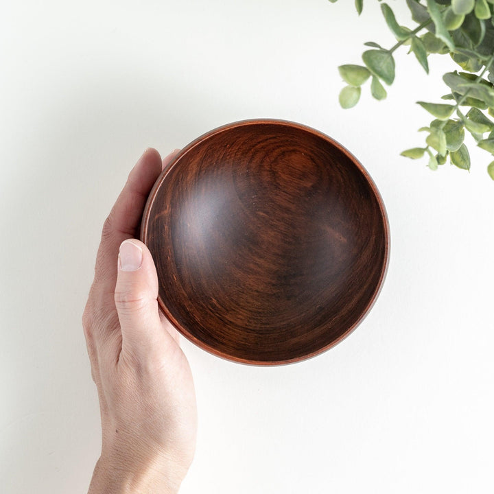 A hand holding the handcrafted brown wooden bowl, showcasing its sleek interior and natural wood finish.