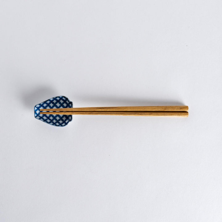 Chopsticks placed on the blue geometric vase-shaped sauce dish with a flower pattern, showcasing its unique design.