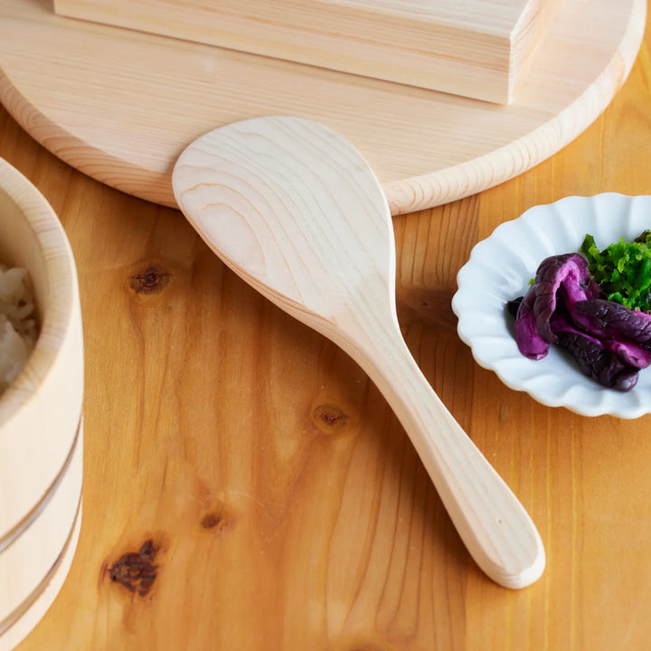 Hinoki wood rice paddle placed beside fresh cooked rice and Japanese pickles on a wooden table for traditional home cooking