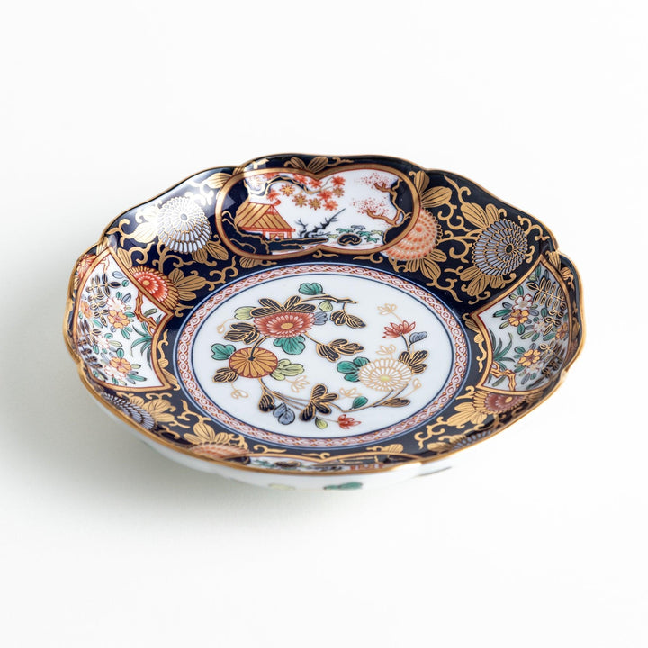 A deep round salad plate with a dark blue background, featuring a central floral design and intricate gold and red patterns with small scenes of Japanese landscapes.