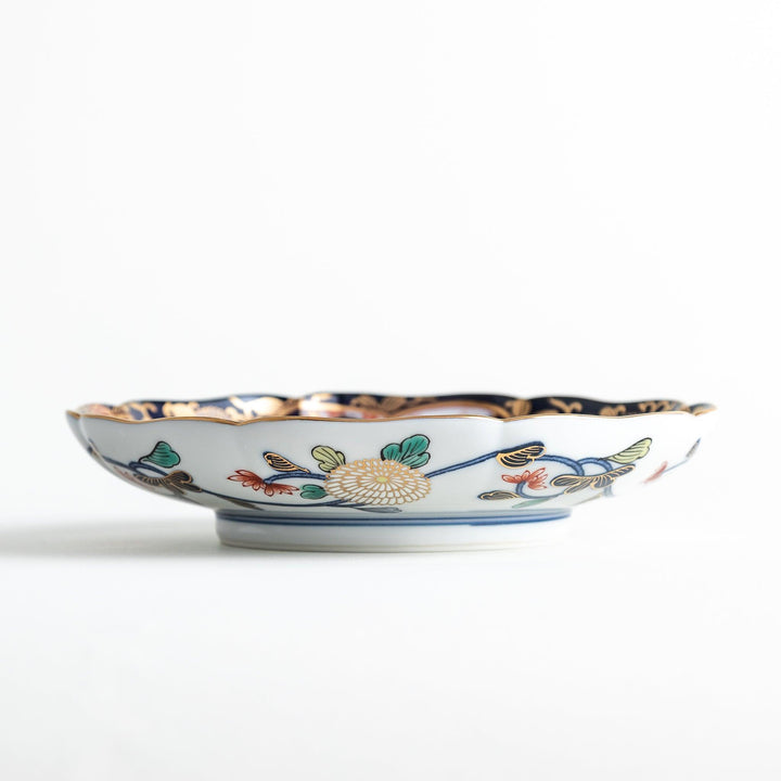 A deep round salad plate with a dark blue background, featuring a central floral design and intricate gold and red patterns with small scenes of Japanese landscapes.
