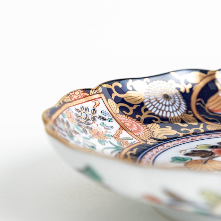 A deep round salad plate with a dark blue background, featuring a central floral design and intricate gold and red patterns with small scenes of Japanese landscapes.