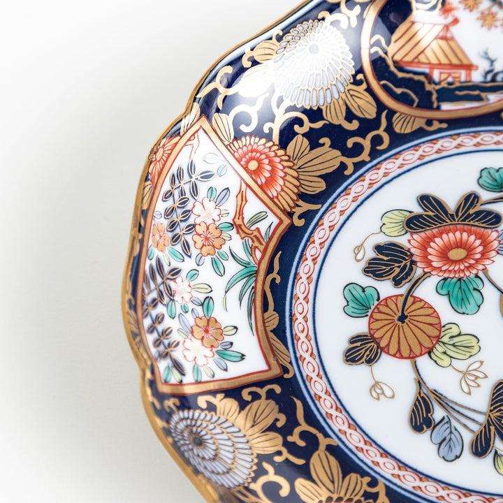 A deep round salad plate with a dark blue background, featuring a central floral design and intricate gold and red patterns with small scenes of Japanese landscapes.