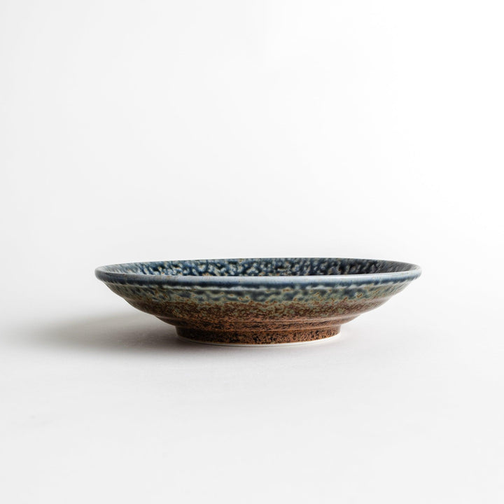 A pasta bowl with a textured glaze in blue, brown, and cream hues, featuring a ridged interior.