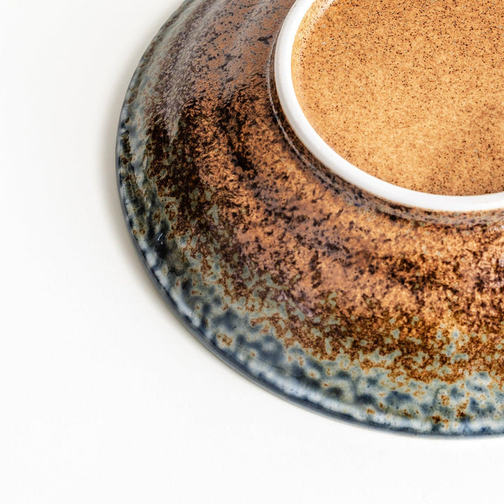 A pasta bowl with a textured glaze in blue, brown, and cream hues, featuring a ridged interior.