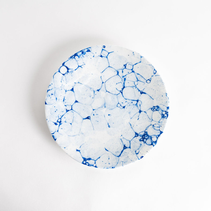 A round dinner plate with a blue bubble-like design on a white background.