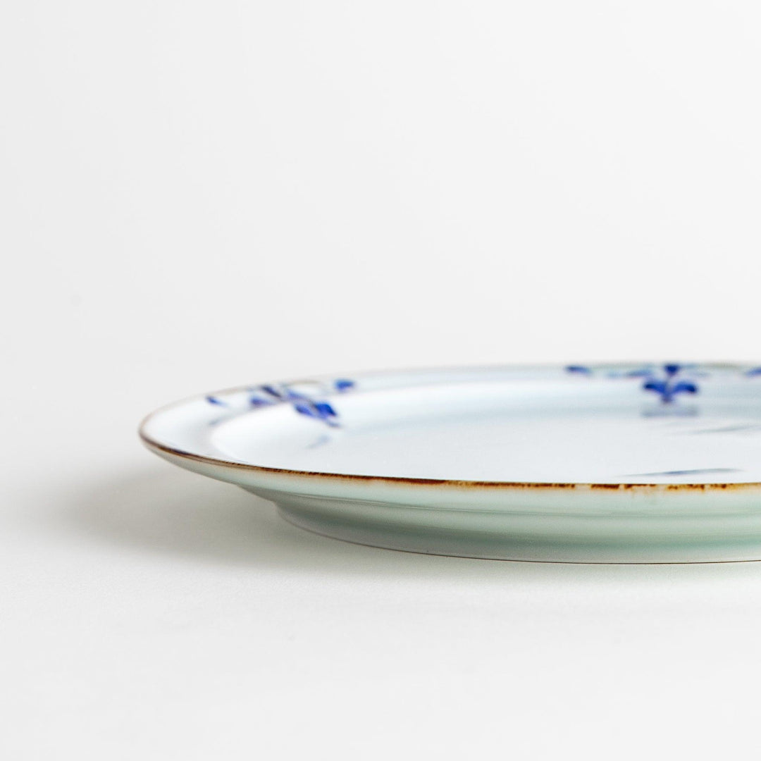 A small porcelain salad plate with a scalloped edge, decorated with blue and white floral motifs and brown accent trim.