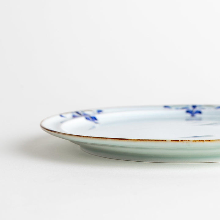A small porcelain salad plate with a scalloped edge, decorated with blue and white floral motifs and brown accent trim.