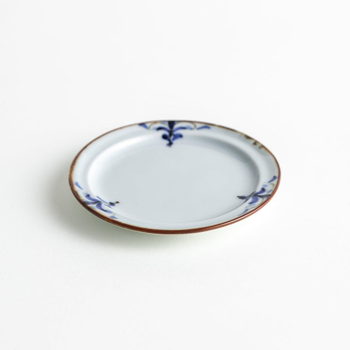 A small porcelain sauce dish with a scalloped edge, featuring a blue and white design of flowers and leaves and brown accent trim.