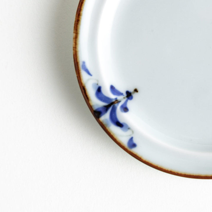 A small porcelain sauce dish with a scalloped edge, featuring a blue and white design of flowers and leaves and brown accent trim.