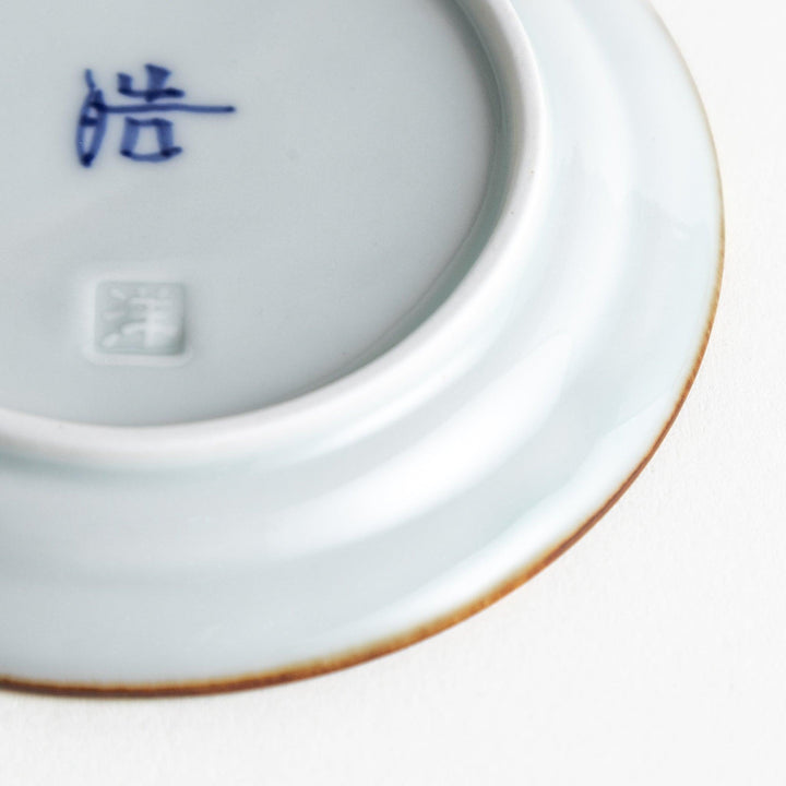 A small porcelain sauce dish with a scalloped edge, featuring a blue and white design of flowers and leaves and brown accent trim.