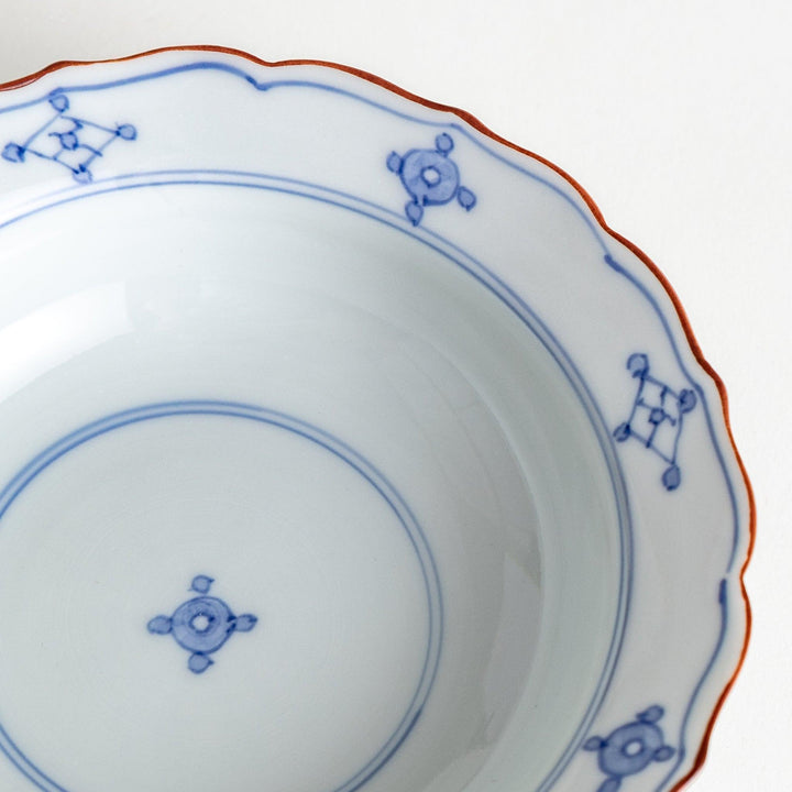 A ceramic bowl featuring a blue geometric motif and scalloped edges.