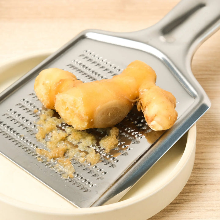 Grating fresh ginger on a Shark Skin Stainless Steel Wasabi Grater, perfect for creating smooth, aromatic pastes for cooking.