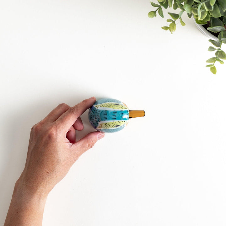 A bird-shaped ceramic soy sauce dispenser with vibrant patterns in turquoise, yellow, and green.