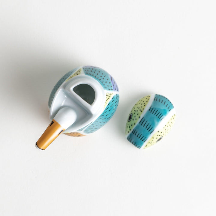 A bird-shaped ceramic soy sauce dispenser with vibrant patterns in turquoise, yellow, and green.