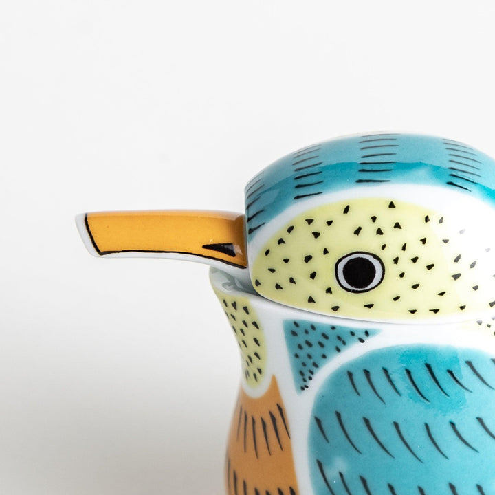 A bird-shaped ceramic soy sauce dispenser with vibrant patterns in turquoise, yellow, and green.