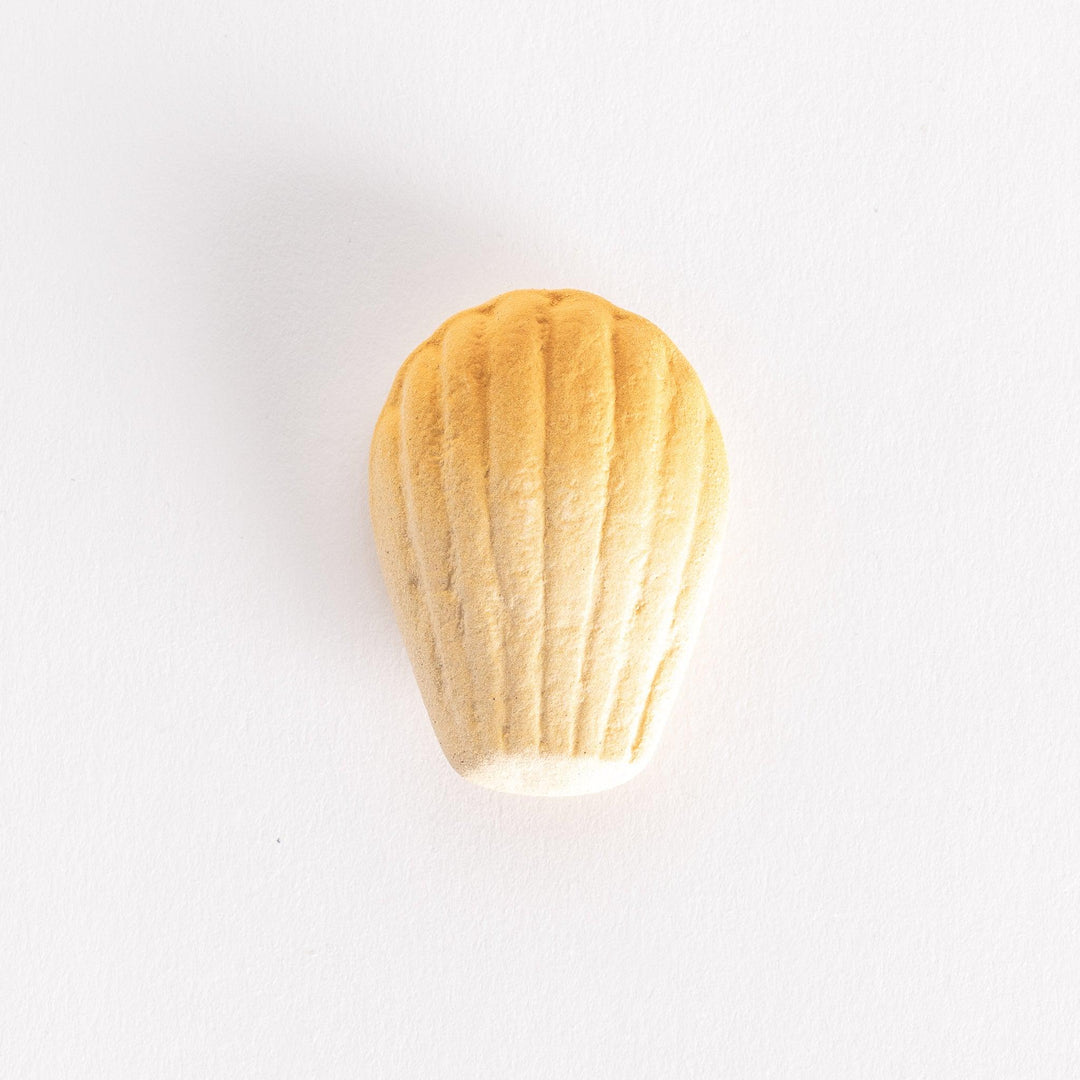 A ceramic chopstick rest shaped like a golden madeleine, showcasing its textured ridges on a white background.