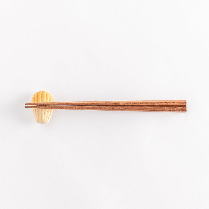 A wide view of the ceramic golden madeleine chopstick rest with chopsticks placed on it, emphasizing its elegant design and soft tones.