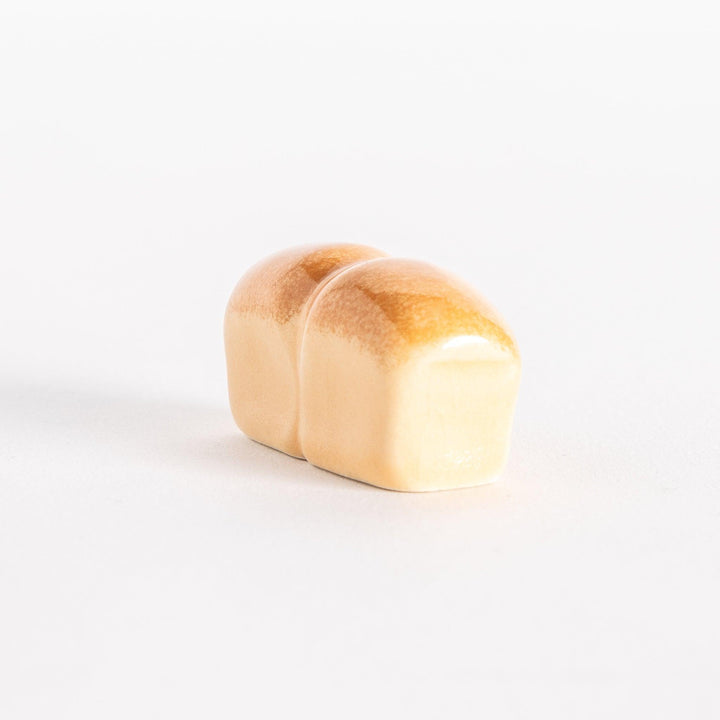 A ceramic chopsticks rest shaped like a loaf of milk bread with a glossy golden-brown top.