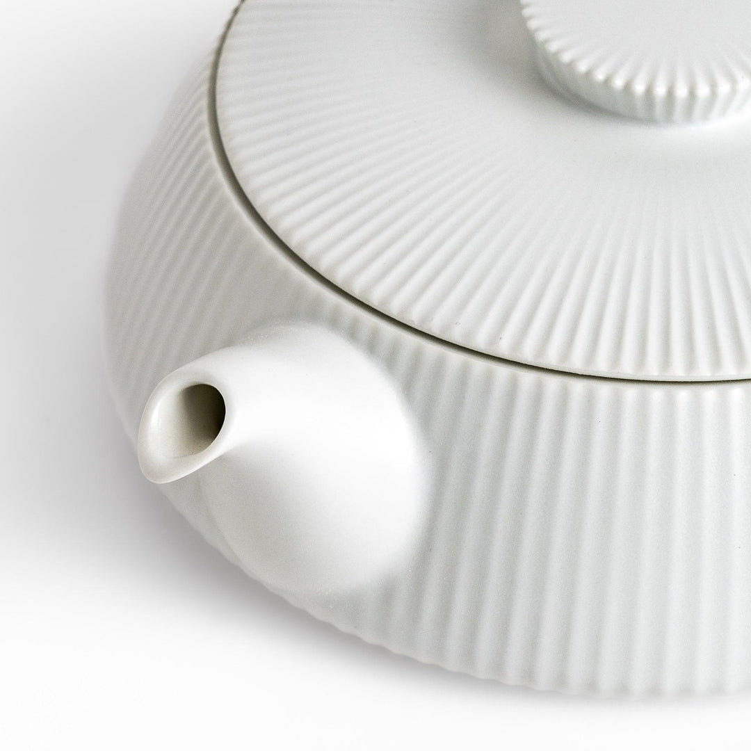 Minimalist ribbed white teapot with a sleek spout and a simple, elegant design, featuring a round lid with a textured top for a modern touch to your tea set.