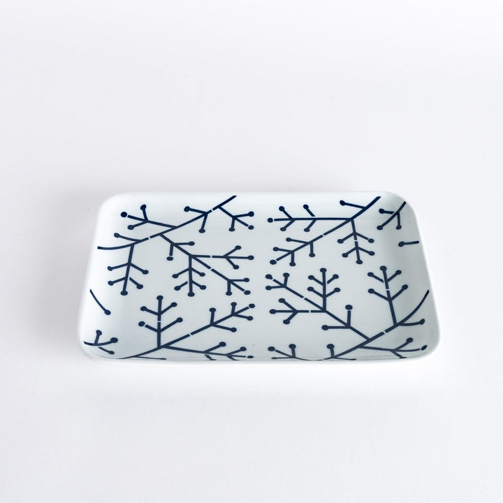 Slightly angled view of the Modern Indigo Pine Dinner Plate held in hand, highlighting the delicate navy blue pine branch pattern on a white surface.