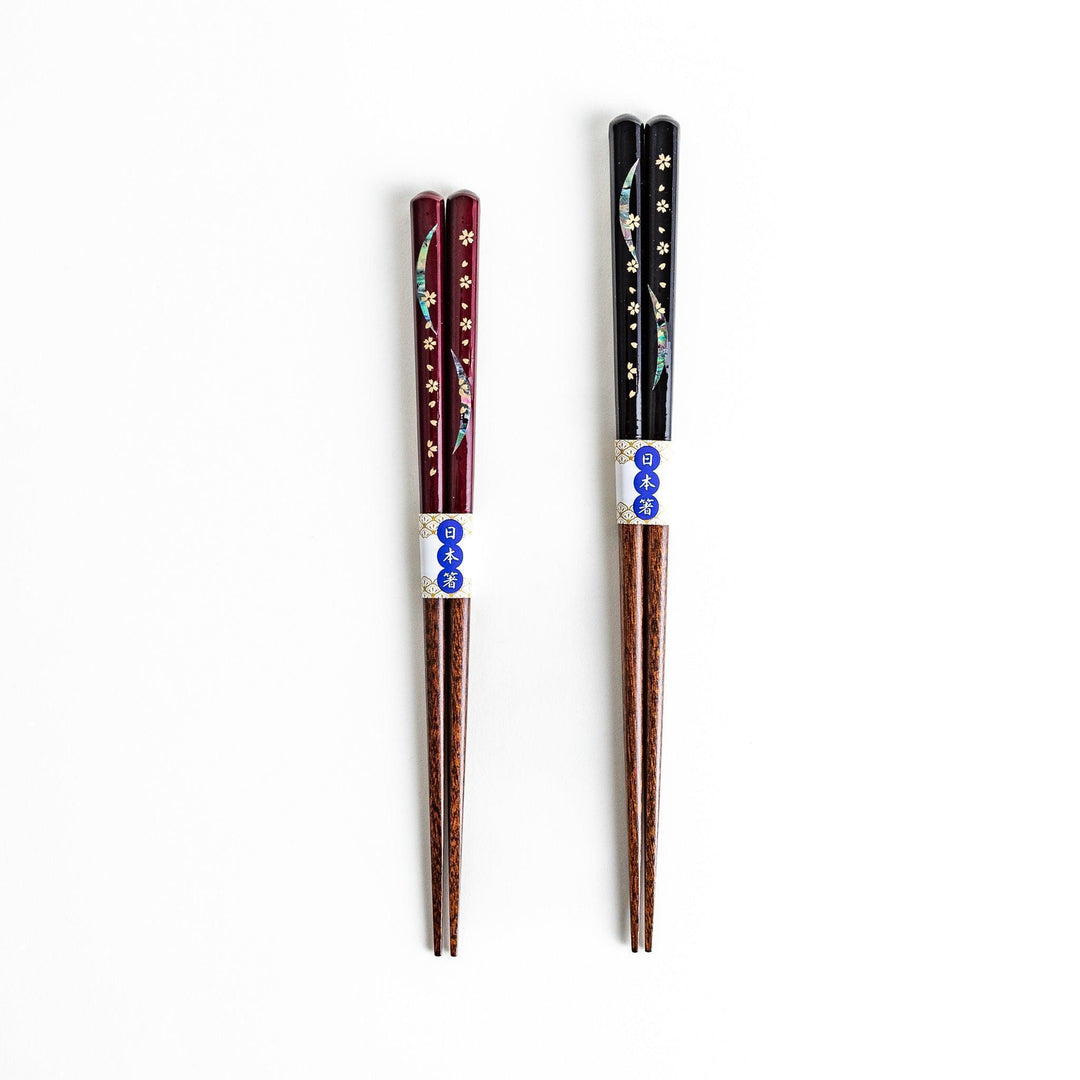 Two pairs of chopsticks, one with red and one with black handles, featuring moon and sakura design.
