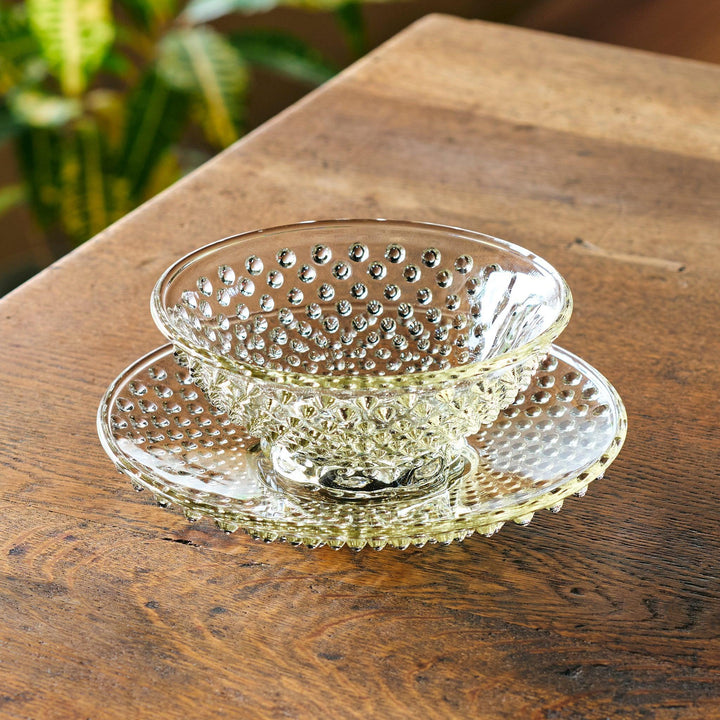 Amber-toned glass dessert bowl and saucer set with raised dot pattern and starburst base, ideal for refined sweets or fruit servings.