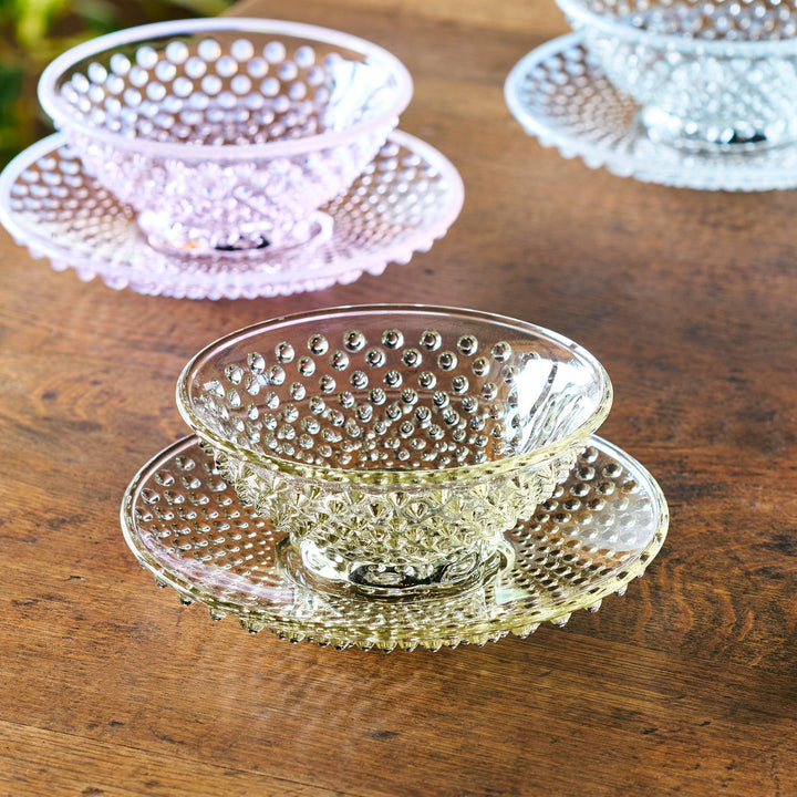 Textured glass dessert bowl and saucer sets in pink, amber, and clear, each with raised dot patterns and a radiant base design.